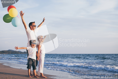 Image of Father and children with balloons playing on the beach at the da
