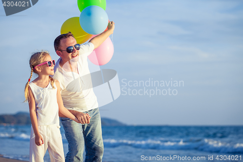 Image of Father and daughter with balloons playing on the beach at the da