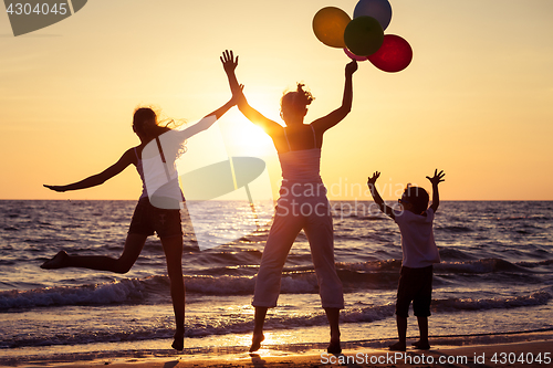 Image of Mother and children playing with balloons on the beach at the su