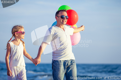 Image of Father and daughter with balloons playing on the beach at the da