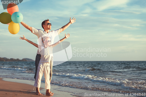 Image of Father and daughter with balloons playing on the beach at the da