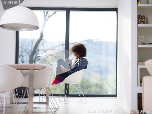 Image of black woman drinking coffee and using a mobile phone  at home