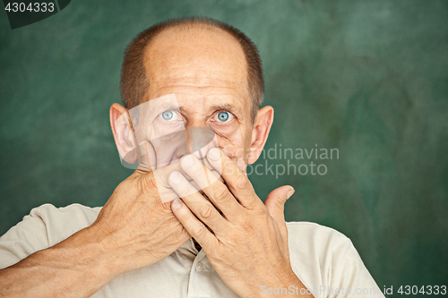 Image of Shocked senior gentleman holding his hand against his mouth and looking at the camera