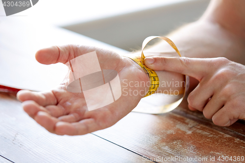 Image of close up of male hands with tape measuring wrist