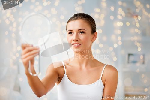 Image of beautiful woman with mirror sitting on bed at home