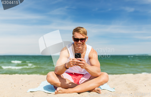 Image of happy smiling young man with smartphone on beach