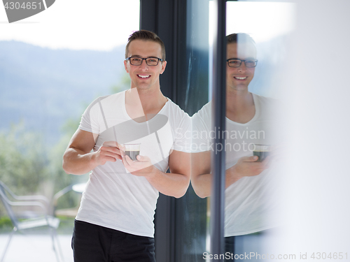 Image of young man drinking morning coffee by the window