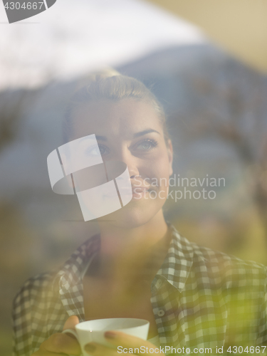 Image of young woman drinking morning coffee by the window