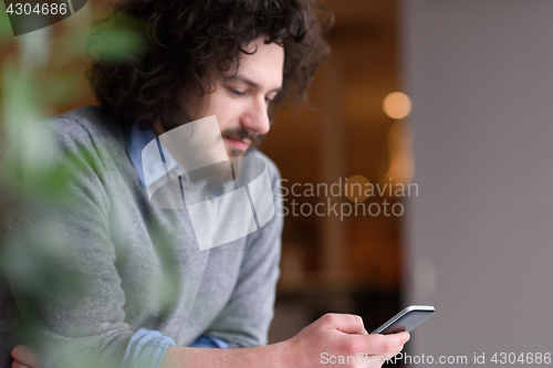 Image of Young casual businessman holding smartphone