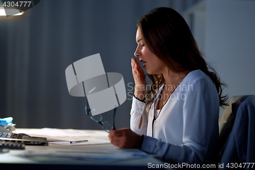 Image of tired woman with glasses yawning at night office