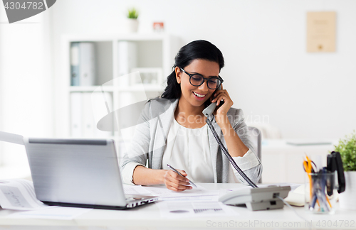 Image of happy businesswoman calling on phone at office