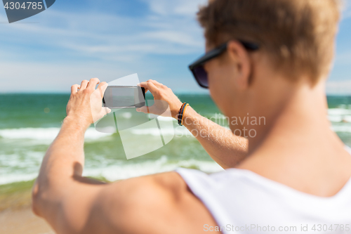 Image of man with smartphone photographing on summer beach