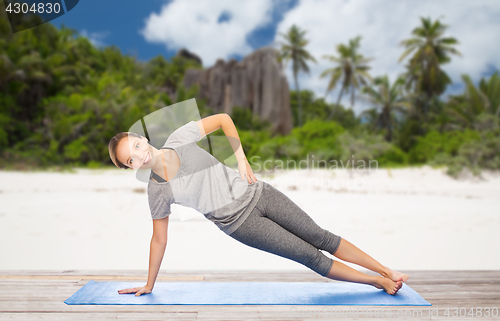 Image of woman doing yoga in side plank pose on beach