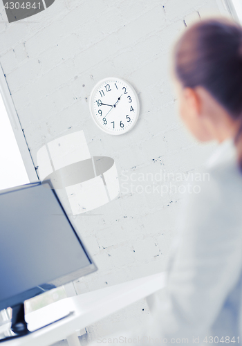 Image of businesswoman looking at wall clock in office