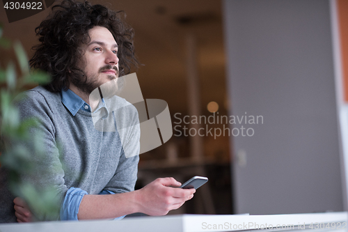 Image of Young casual businessman holding smartphone