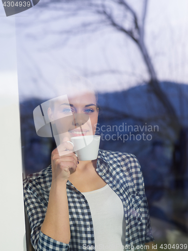 Image of young woman drinking morning coffee by the window