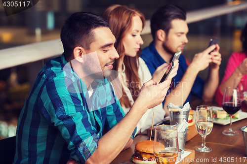 Image of friends with smartphones dining at restaurant