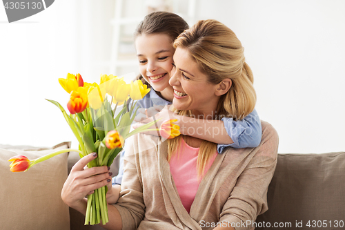 Image of happy girl giving flowers to mother at home