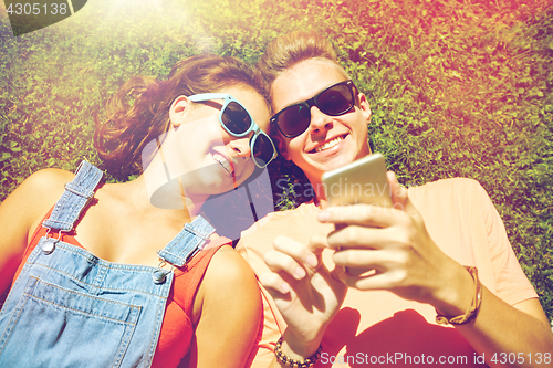 Image of happy teenage couple smartphone lying on grass