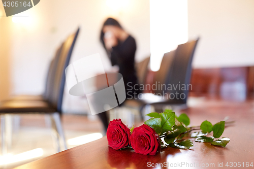 Image of red roses and woman crying at funeral in church