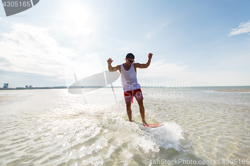 Image of young man riding on skimboard on summer beach