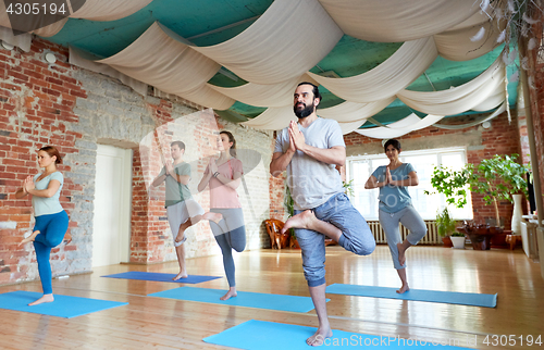 Image of group of people doing yoga tree pose at studio