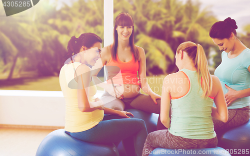 Image of happy pregnant women sitting on balls in gym