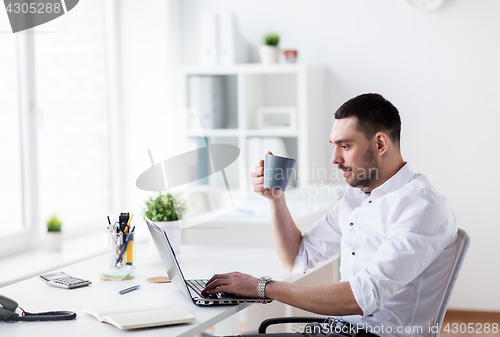 Image of businessman with coffee typing on laptop at office