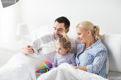Image of happy family with smartphone in bed at home