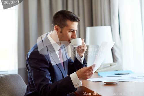 Image of businessman with papers drinking coffee at hotel