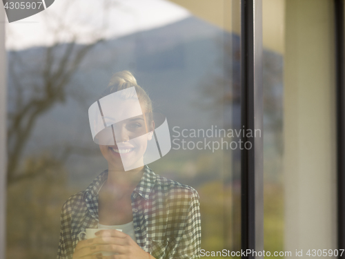 Image of young woman drinking morning coffee by the window