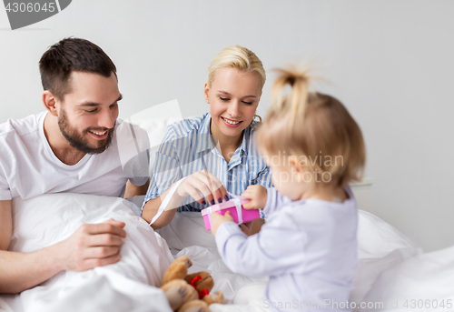 Image of happy family with gift box in bed at home