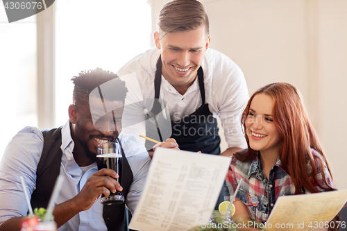 Image of waiter and couple with menu and drinks at bar