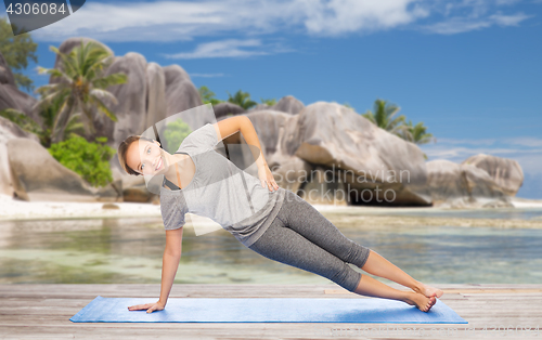 Image of woman doing yoga in side plank pose on beach