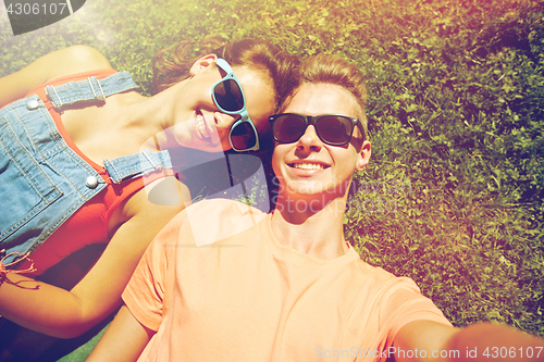 Image of happy teenage couple taking selfie on summer grass