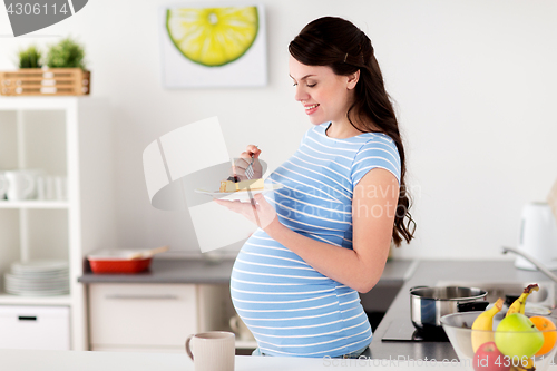 Image of happy pregnant woman eating cake at home kitchen