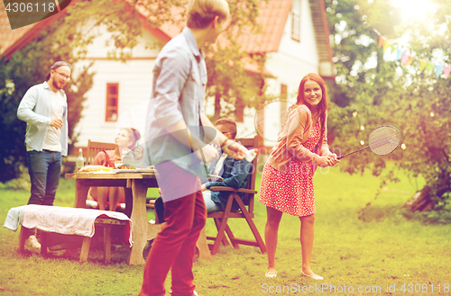 Image of happy friends playing badminton at summer garden