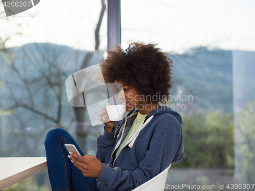 Image of black woman drinking coffee and using a mobile phone  at home