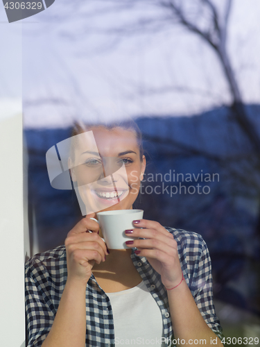 Image of young woman drinking morning coffee by the window