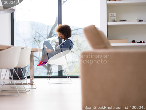 Image of black woman drinking coffee and using a mobile phone  at home