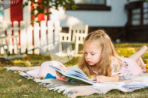 Image of Cute Little Blond Girl Reading Book Outside on Grass