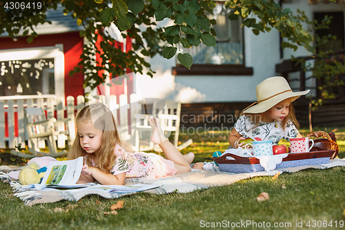 Image of Cute Little Blond Girls Reading Book Outside on Grass