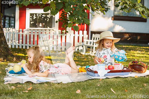 Image of Cute Little Blond Girls Reading Book Outside on Grass