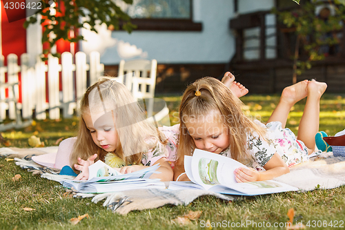 Image of Cute Little Blond Girls Reading Book Outside on Grass