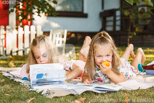 Image of Cute Little Blond Girls Reading Book Outside on Grass