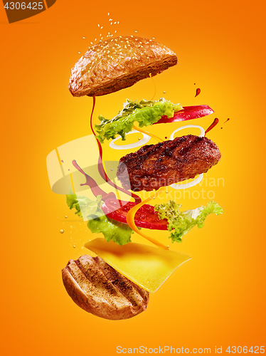 Image of The hamburger with flying ingredients on orange background