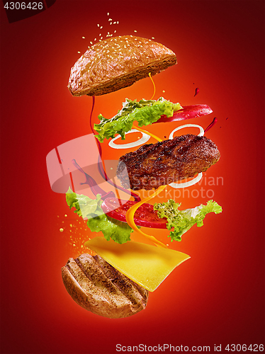 Image of The hamburger with flying ingredients on red background