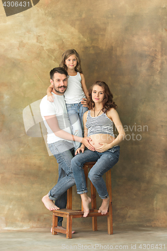 Image of Pregnant mother with teen daughter and husband. Family studio portrait over brown background