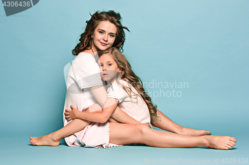 Image of Pregnant mother with teen daughter. Family studio portrait over blue background