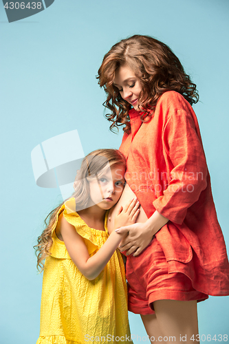 Image of Pregnant mother with teen daughter. Family studio portrait over blue background